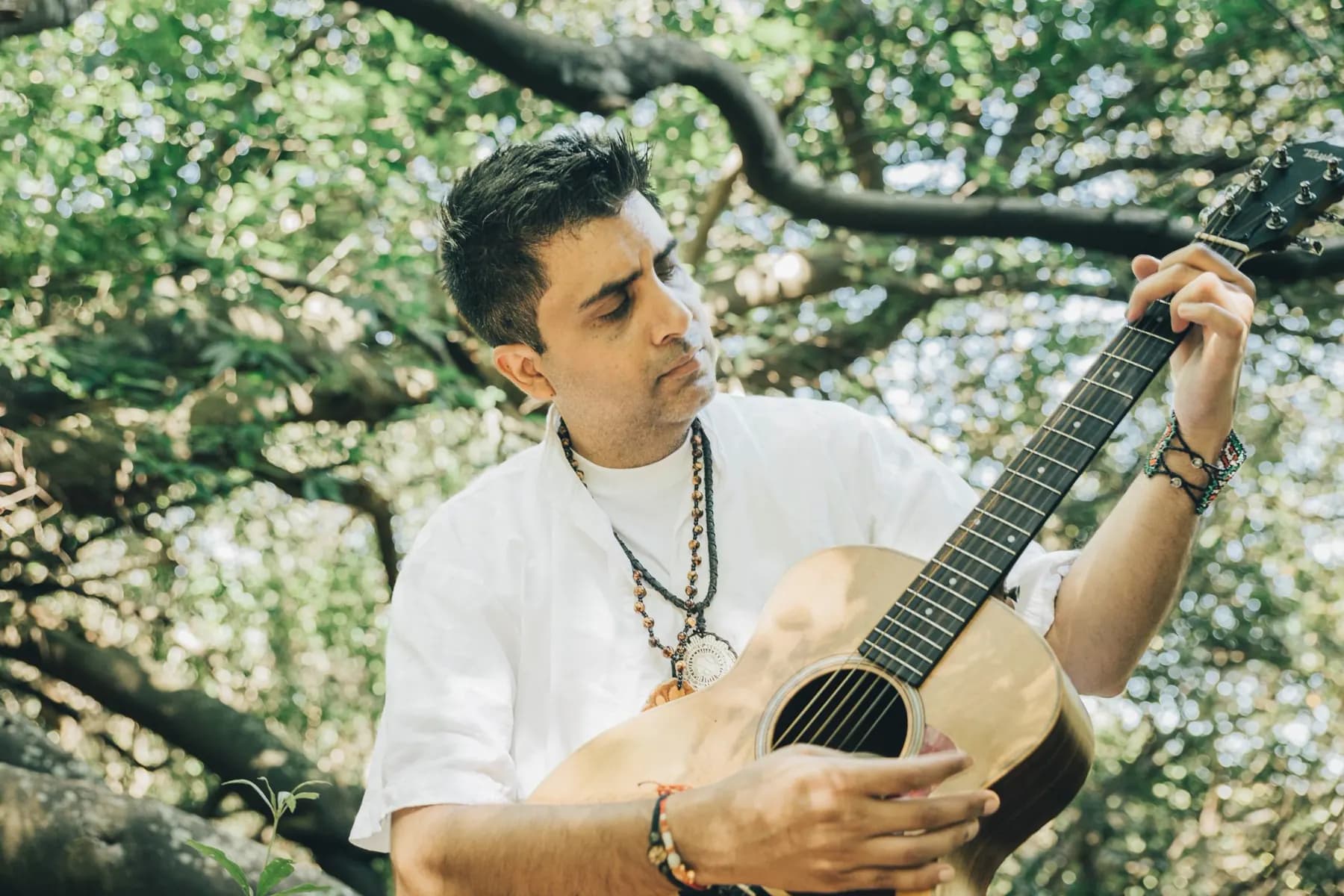 Jayesh Mitha (MINJAY) playing medicine music on guitar beneath the trees